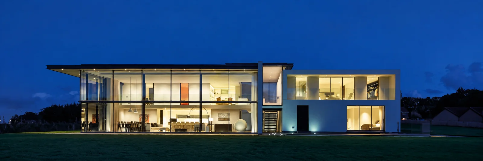Contemporary home with two-storey structural glazing and sliding glass doors at dusk