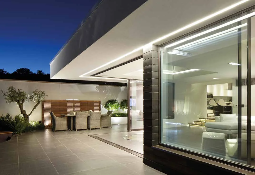 Frameless glass to glass sliding doors beside a contemporary terrace at dusk