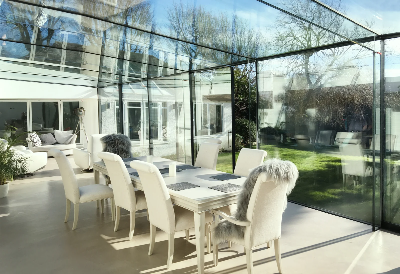Sunlit dining room within frameless glass walls overlooking the garden